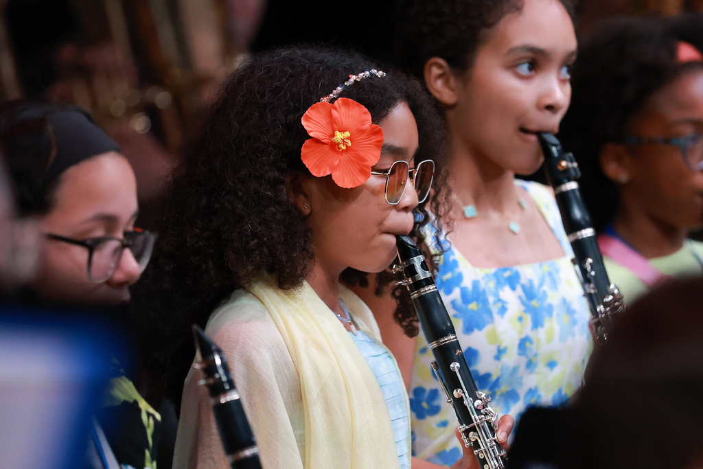 A student plays the clarinet while a flower rests in their hair during a summer musical performance.