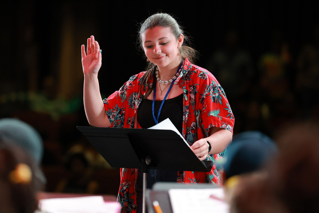A student conducts a symphony band at the front of the stage.