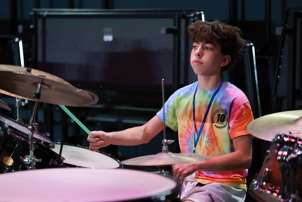 A student plays the drums while wearing a colorful tye-die shirt.