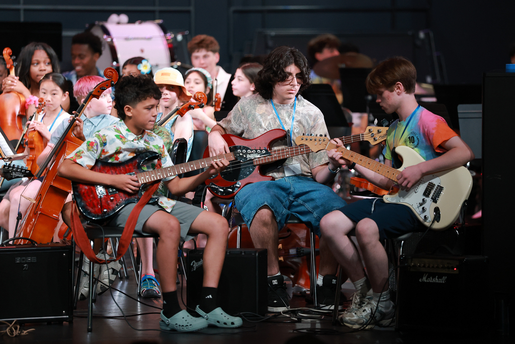 Three students perform with guitars as part of a rock band.
