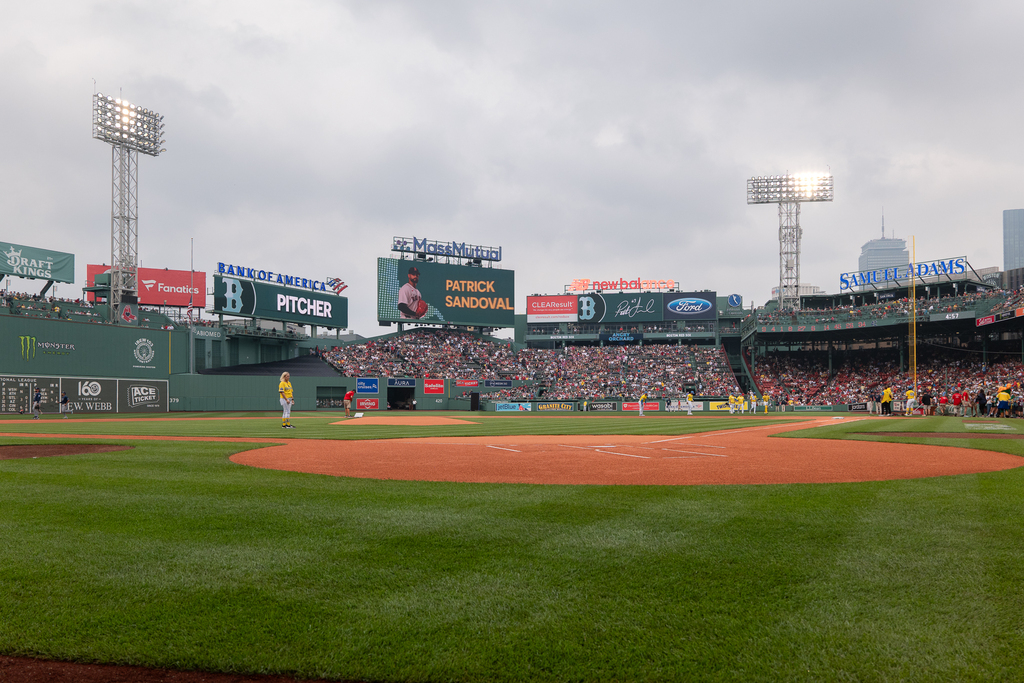 A baseball field with a pitcher on the mound and a crowd in the stands under a cloudy sky.
