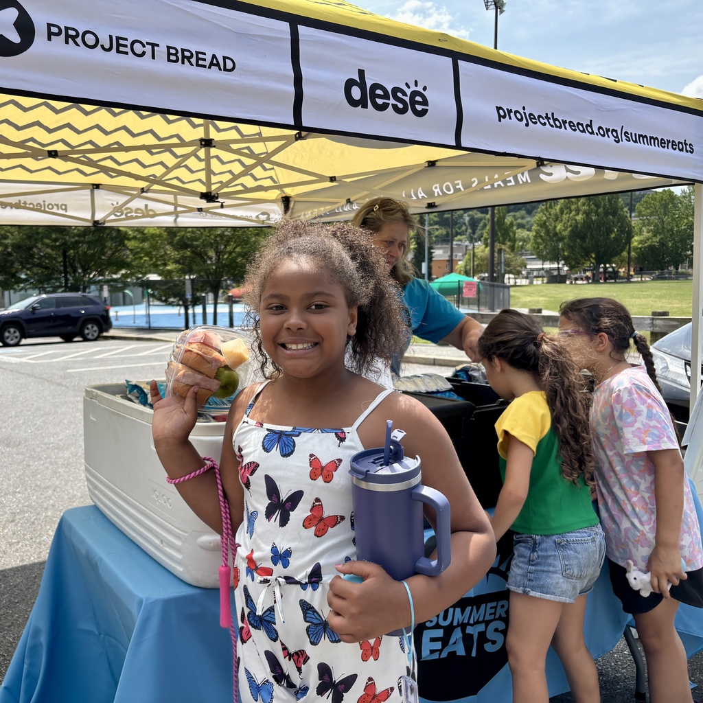 A smiling young girl holds a container of fruit and a purple water bottle in front of a Project Bread tent.