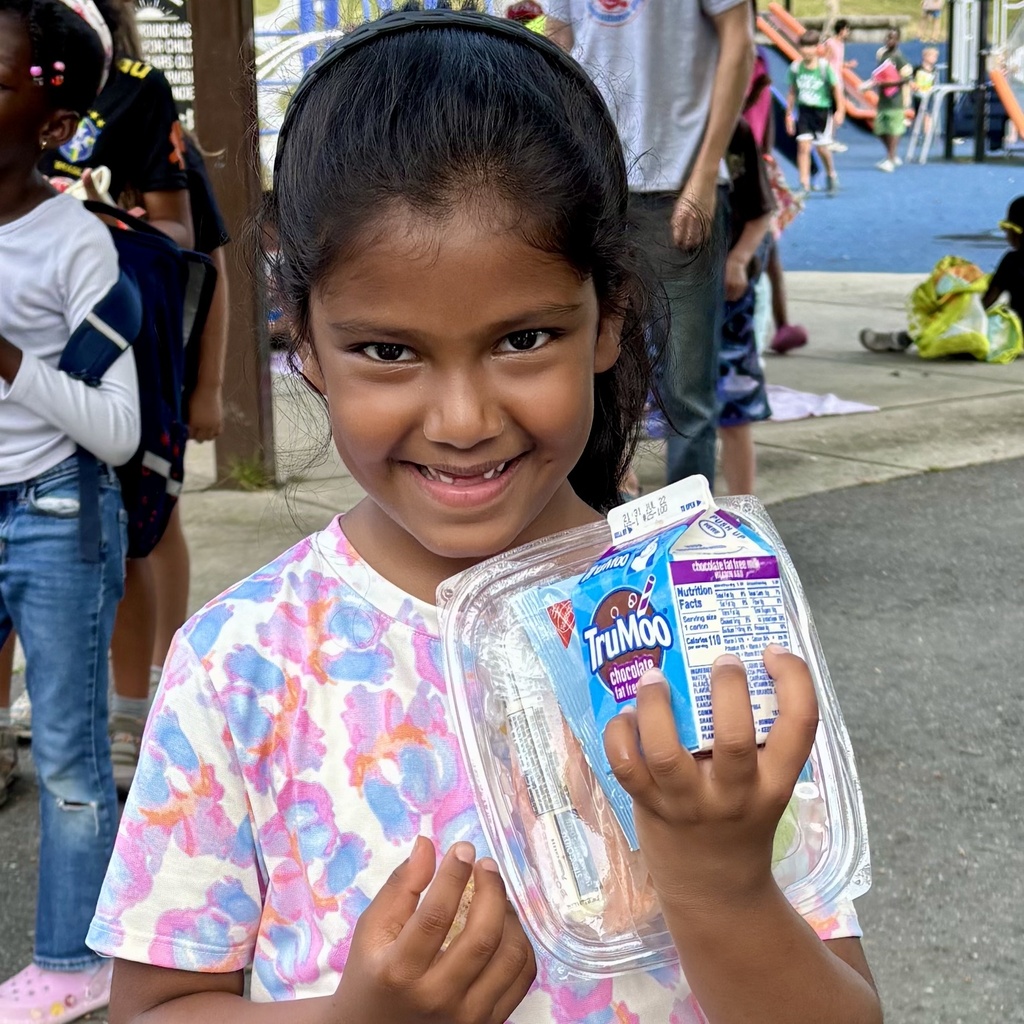 A young girl smiles brightly, holding a container with a carton of TruMoo chocolate milk and a snack.