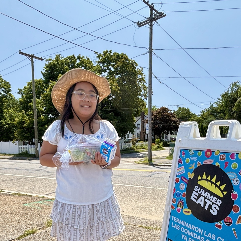A young person wearing a straw hat and glasses holds a container of food and a carton of milk, standing near a "Summer Eats" sign.