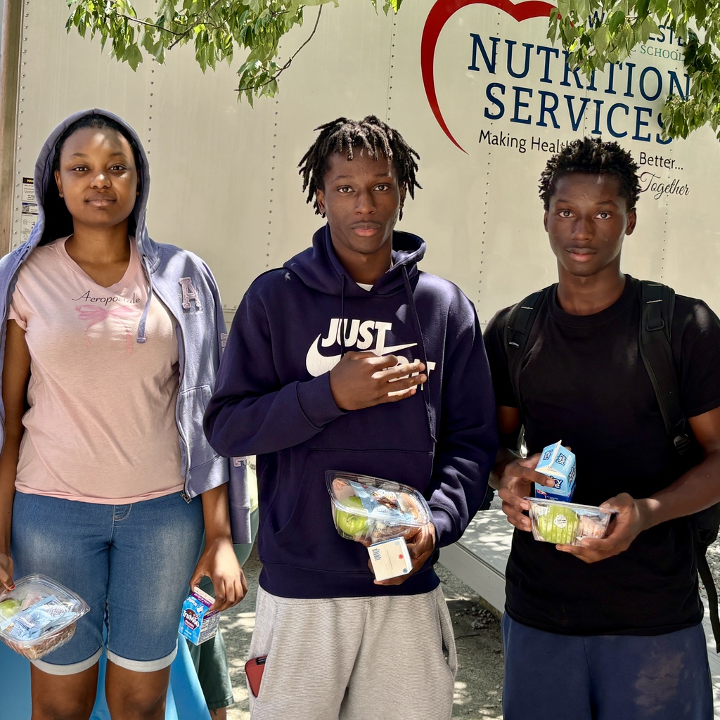 Three young people stand in front of a truck with "Nutrition Services" text, holding food containers and milk cartons.