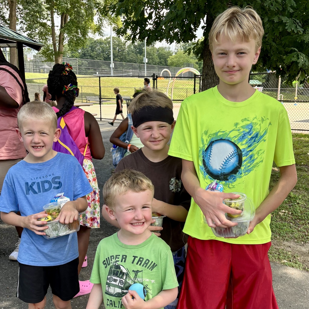Four smiling children stand outdoors, each holding a container of food.
