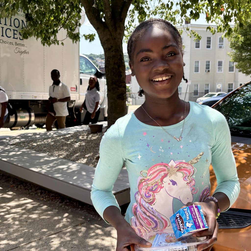 A smiling young girl holds a container of food and a carton of TruMoo chocolate milk.