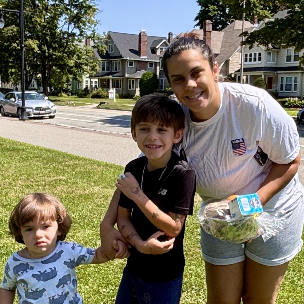 A woman and two young boys smile for a photo outdoors on a sunny day.