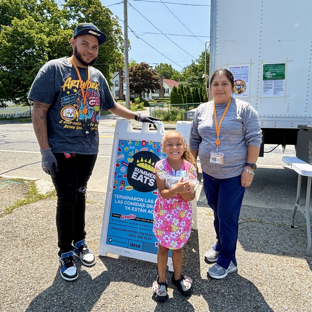 A man, a woman, and a young girl stand next to a sign for "Summer Eats" food program.