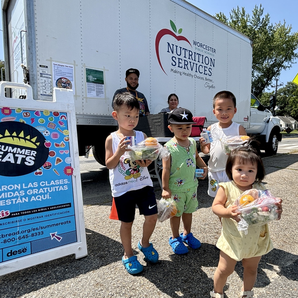 Children hold bags of food in front of a Worcester Nutrition Services truck.