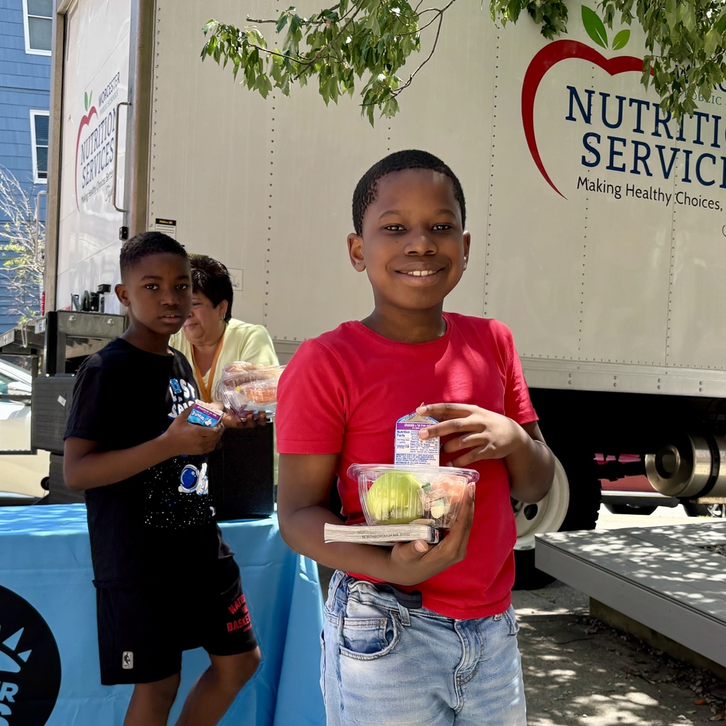 Two young boys stand near a truck with "Worcester Public Schools Nutrition Services" branding, holding lunch items.