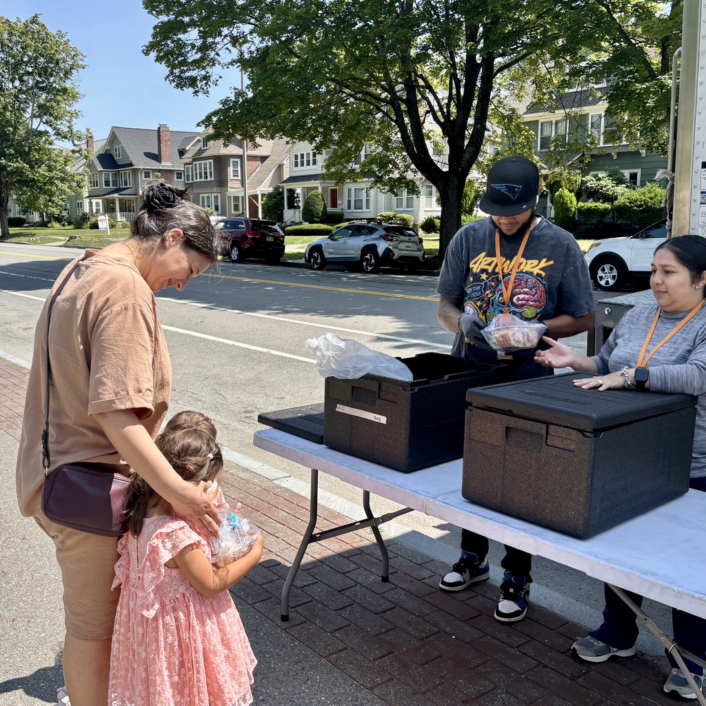 A woman and child receive food from volunteers at an outdoor distribution table.