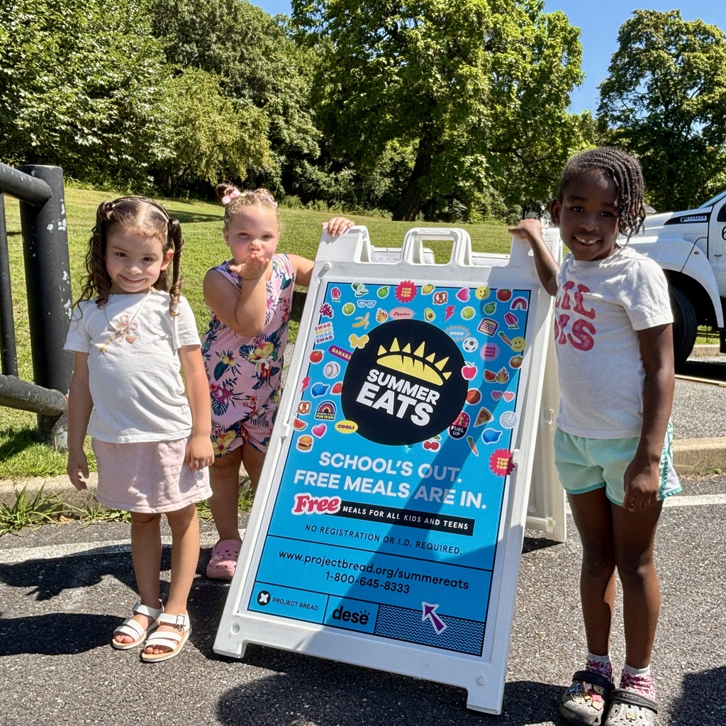Three young girls stand near a sign advertising "Summer Eats" free meals for kids.