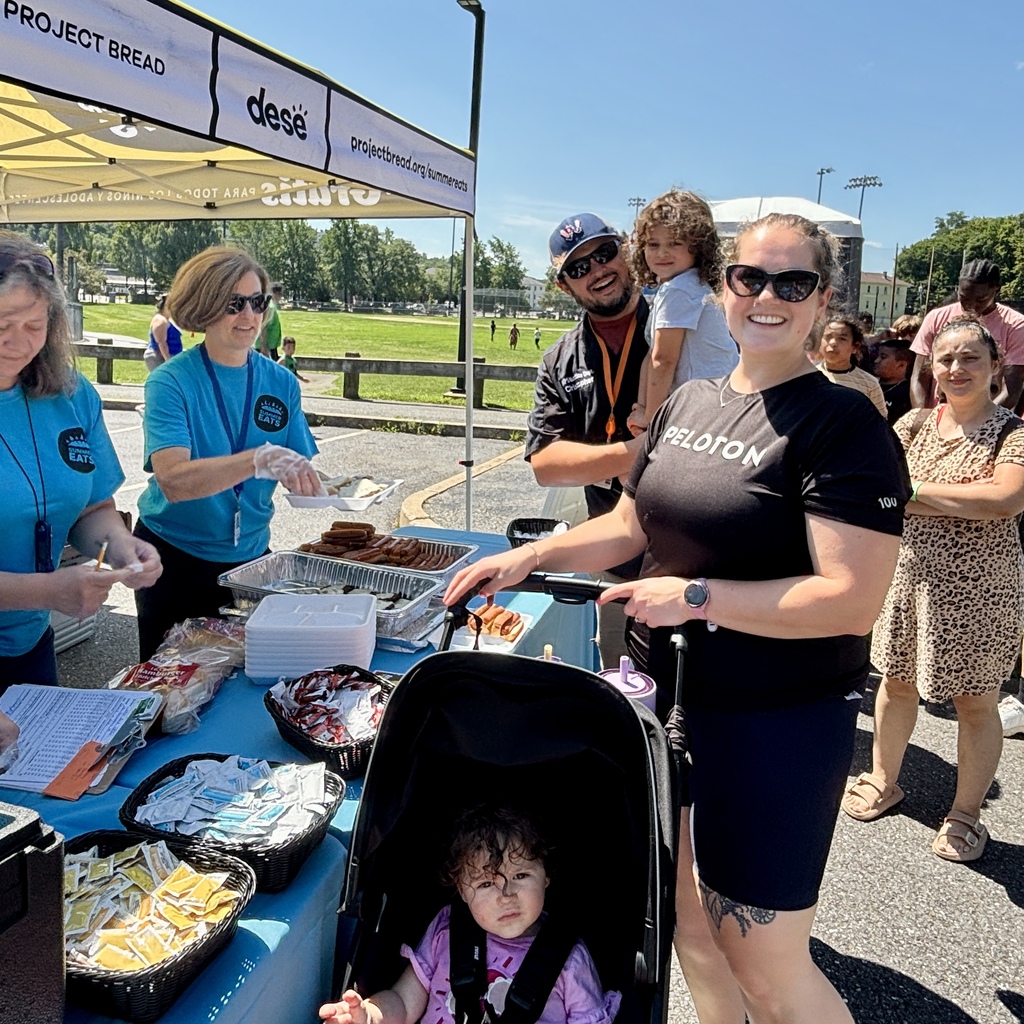 Volunteers serve hot dogs and buns under a tent labeled 'Project Bread' and 'Summer Eats'.