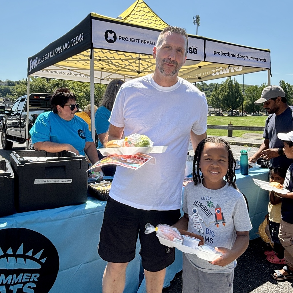 A man and a child smile while holding trays of food at an outdoor event.