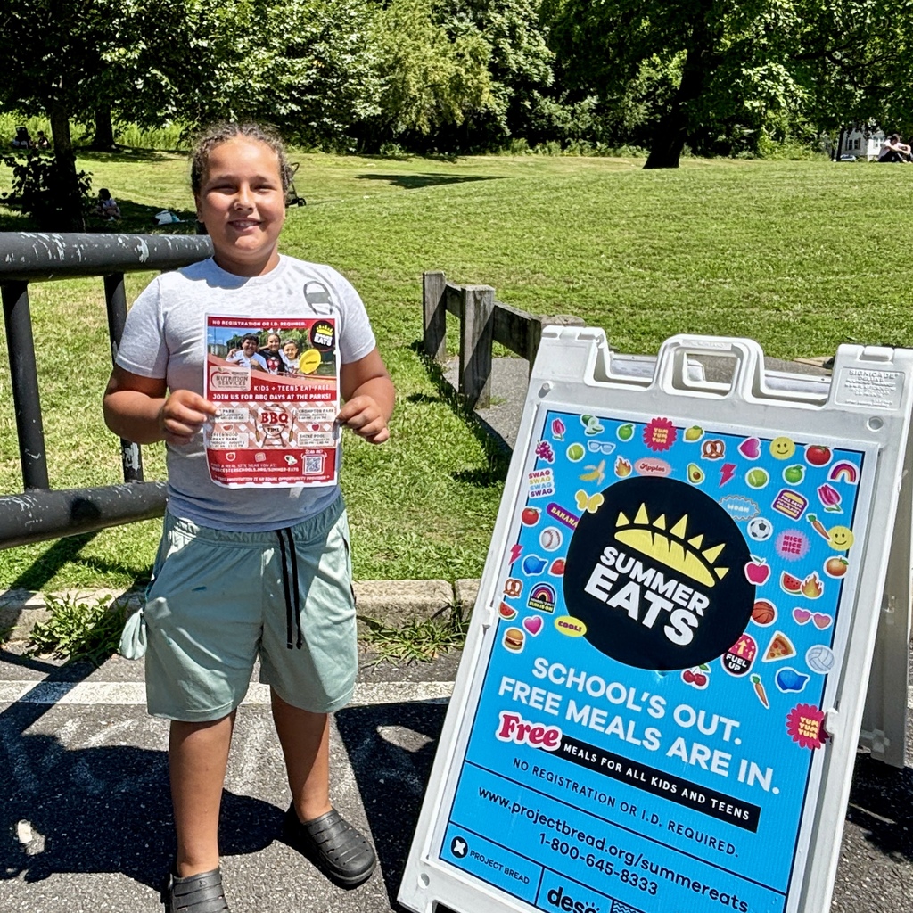 A child holds a flyer for "Summer Eats" program next to a sign advertising free meals for kids and teens.
