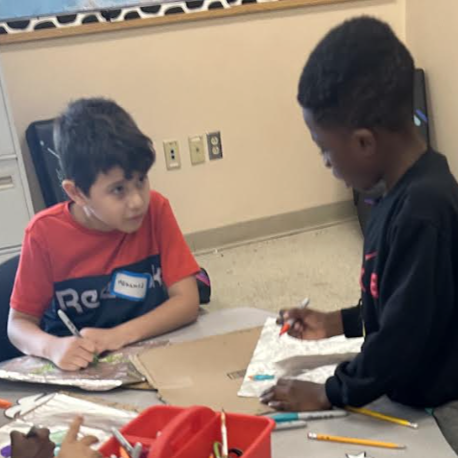 Two young boys are engaged in an art project at a table, drawing and coloring.