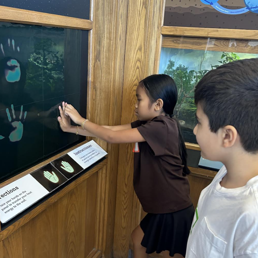 A young girl touches a thermal panel, leaving a handprint, while a boy watches.