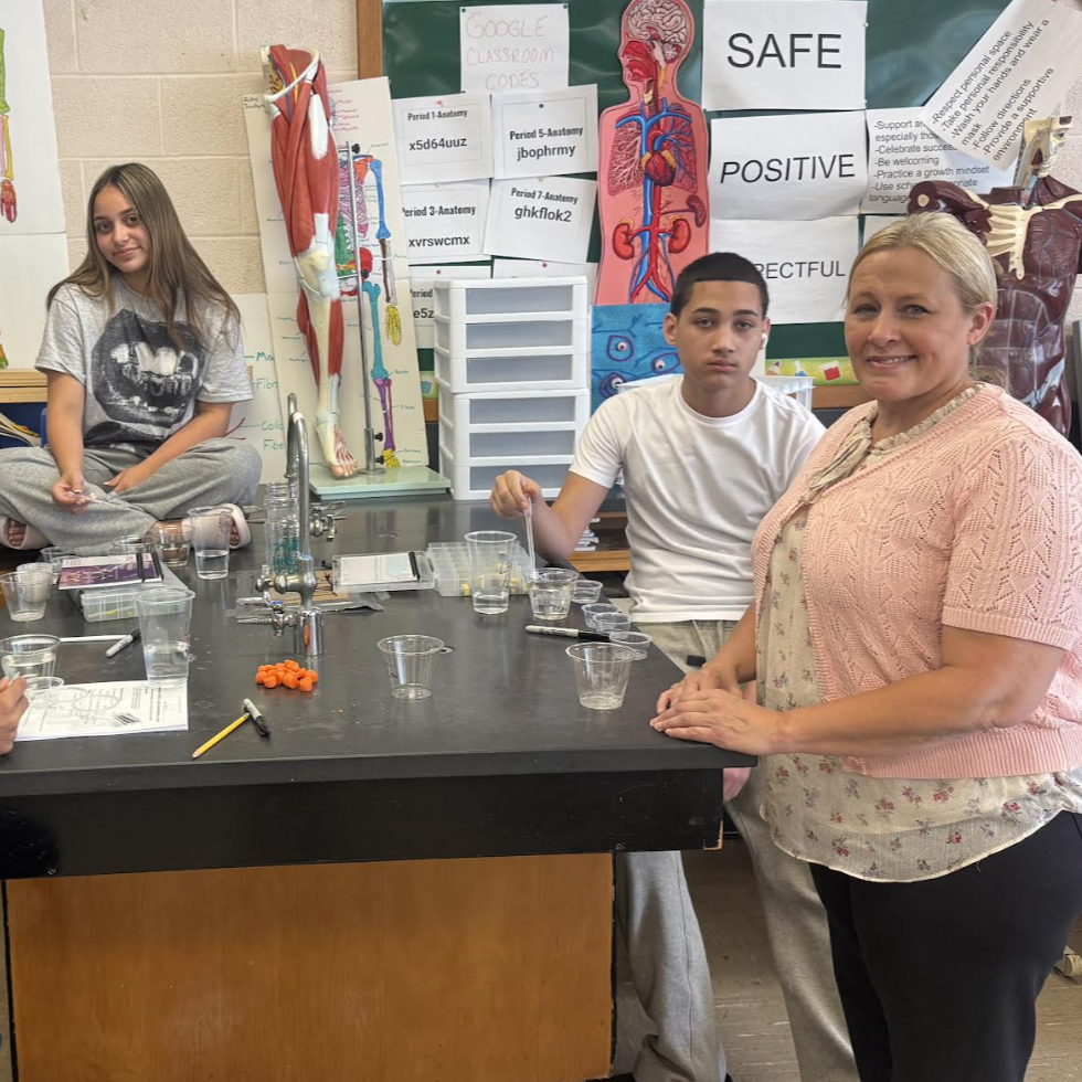 Students and a teacher in a science classroom with anatomical models and lab equipment.