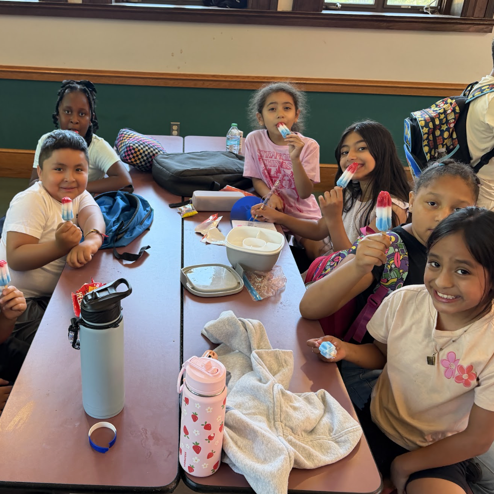 A group of children sit at a table, enjoying popsicles and drinks.