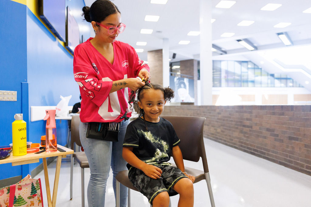 A young boy smilies while he gets his hair braided