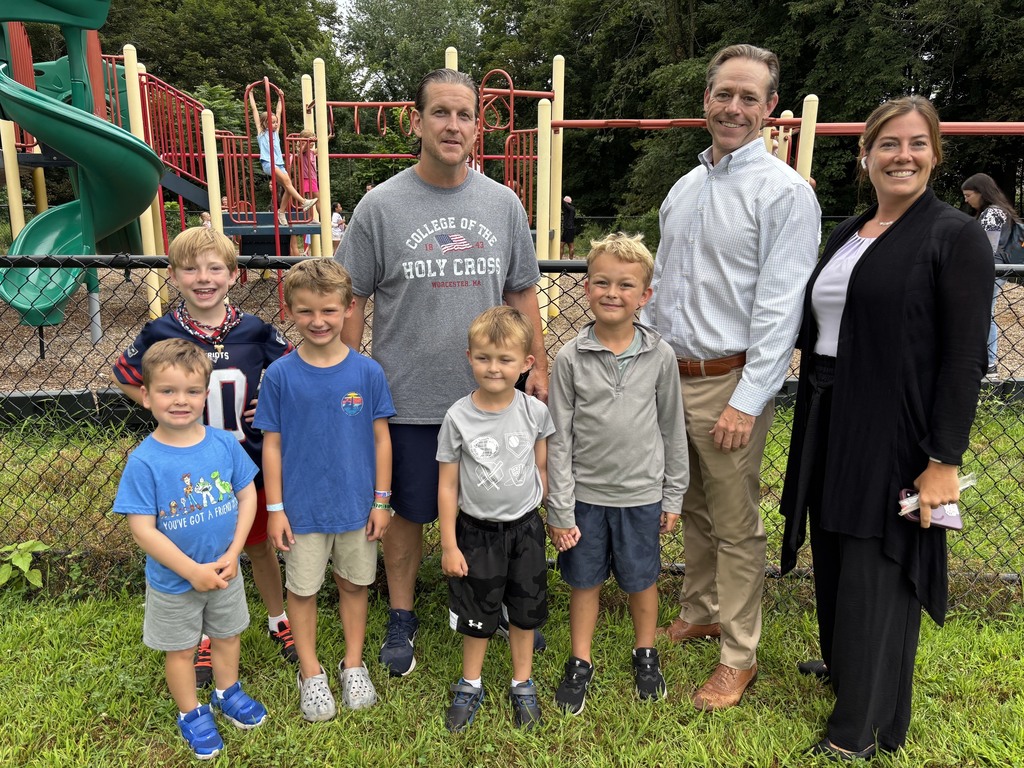 A group of children and adults stand together in front of a playground.