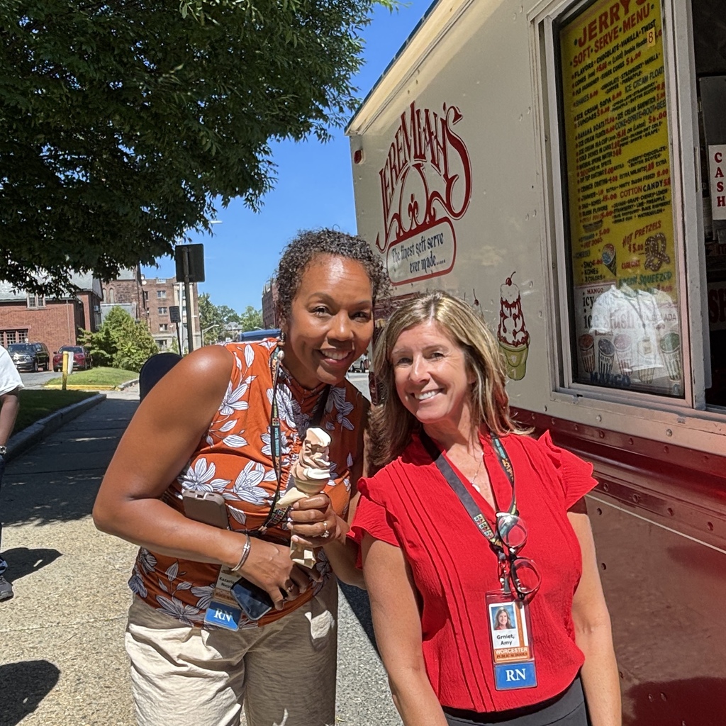 Two women smile in front of an ice cream truck, one holding a soft-serve cone.