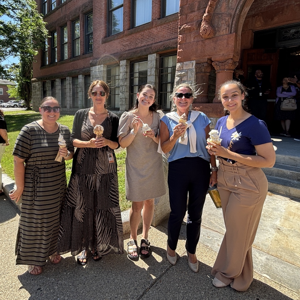 Five smiling women stand outside a brick building, each holding an ice cream cone.