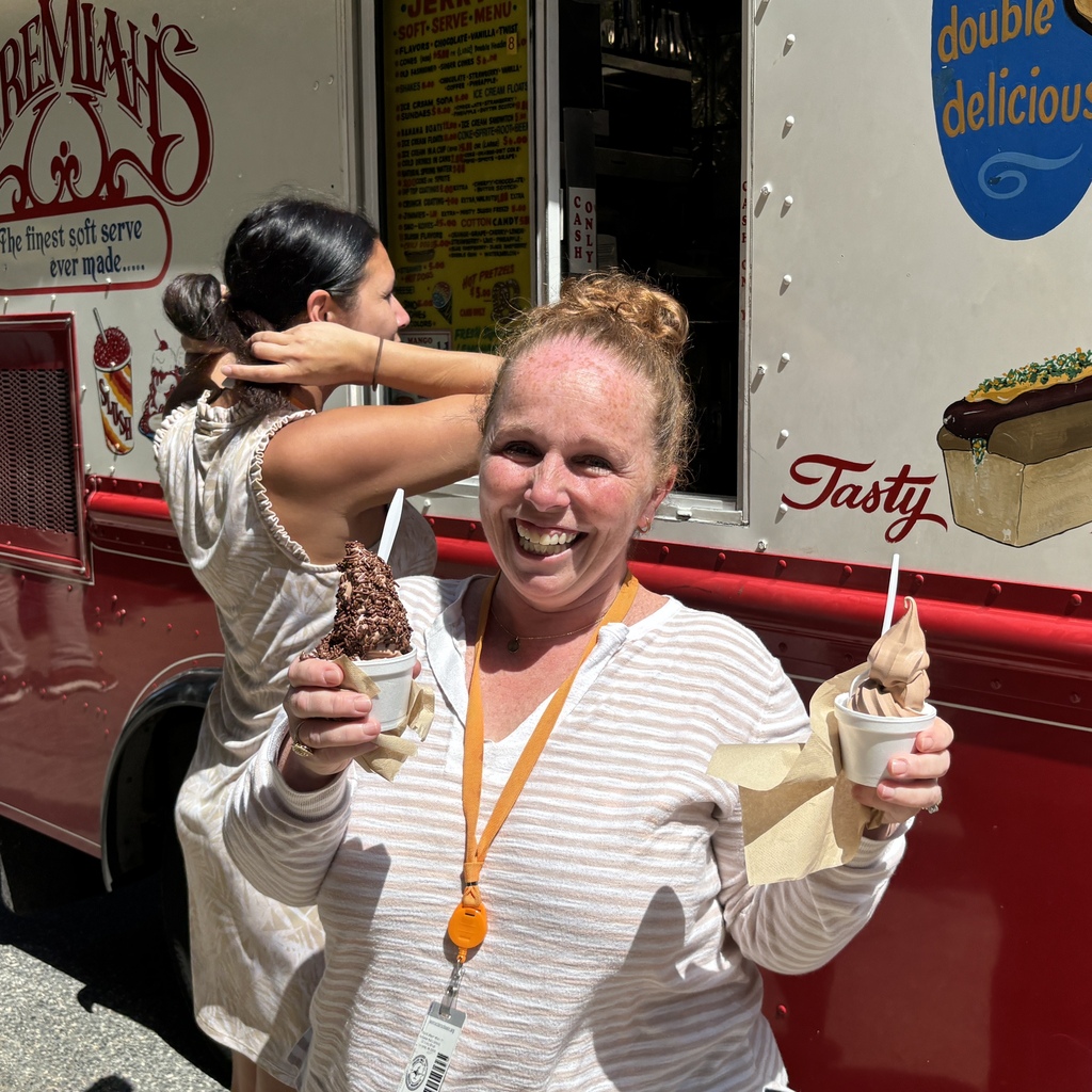 A smiling woman holds two cups of chocolate soft serve ice cream in front of an ice cream truck.