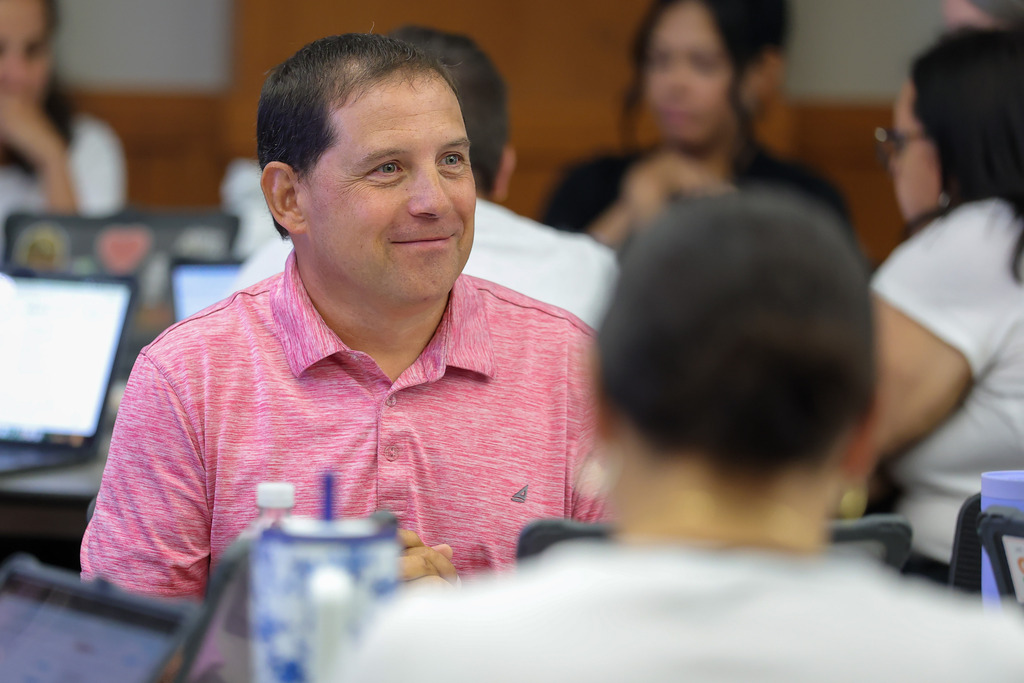 A teacher smiles as he listens to a colleague talk.