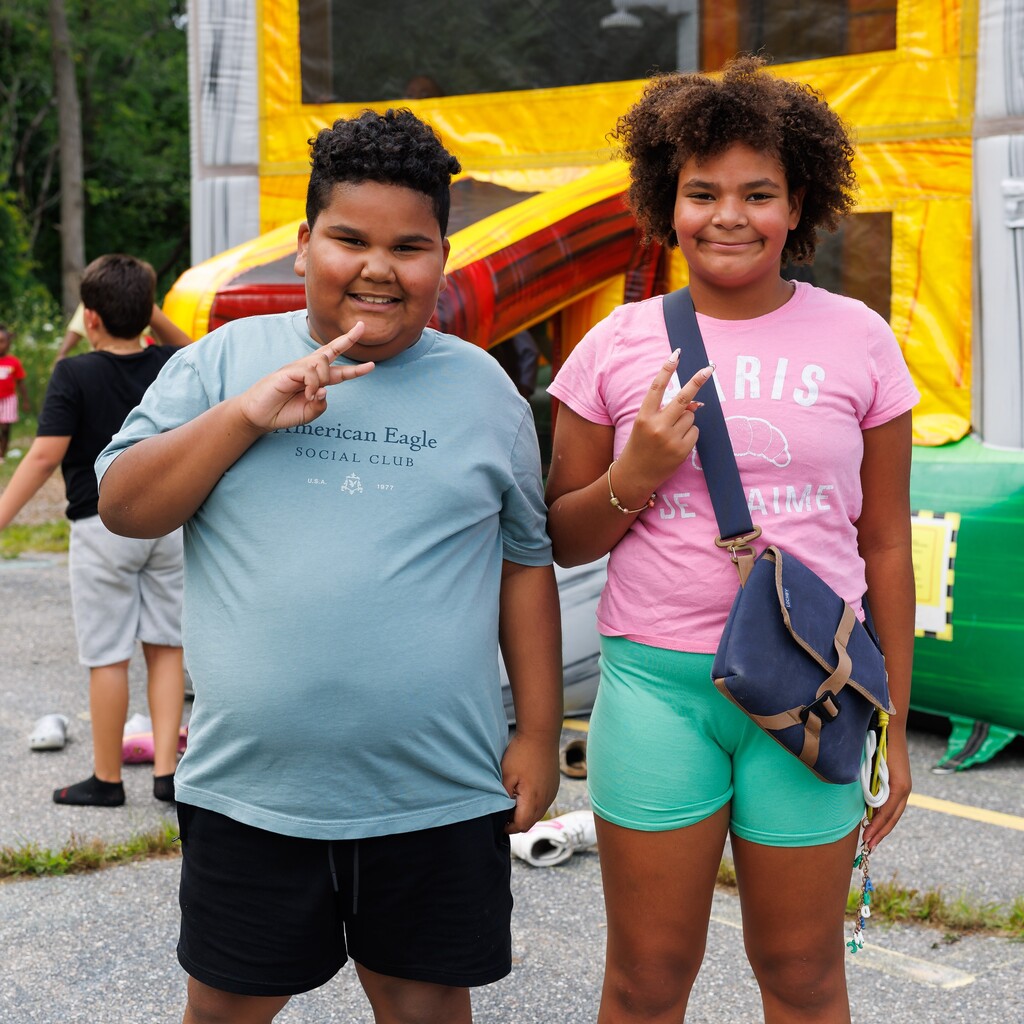Two smiling children pose in front of a large inflatable structure, holding up peace signs.