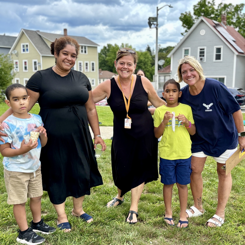 Two women and two children stand together on a grassy lawn with houses in the background.