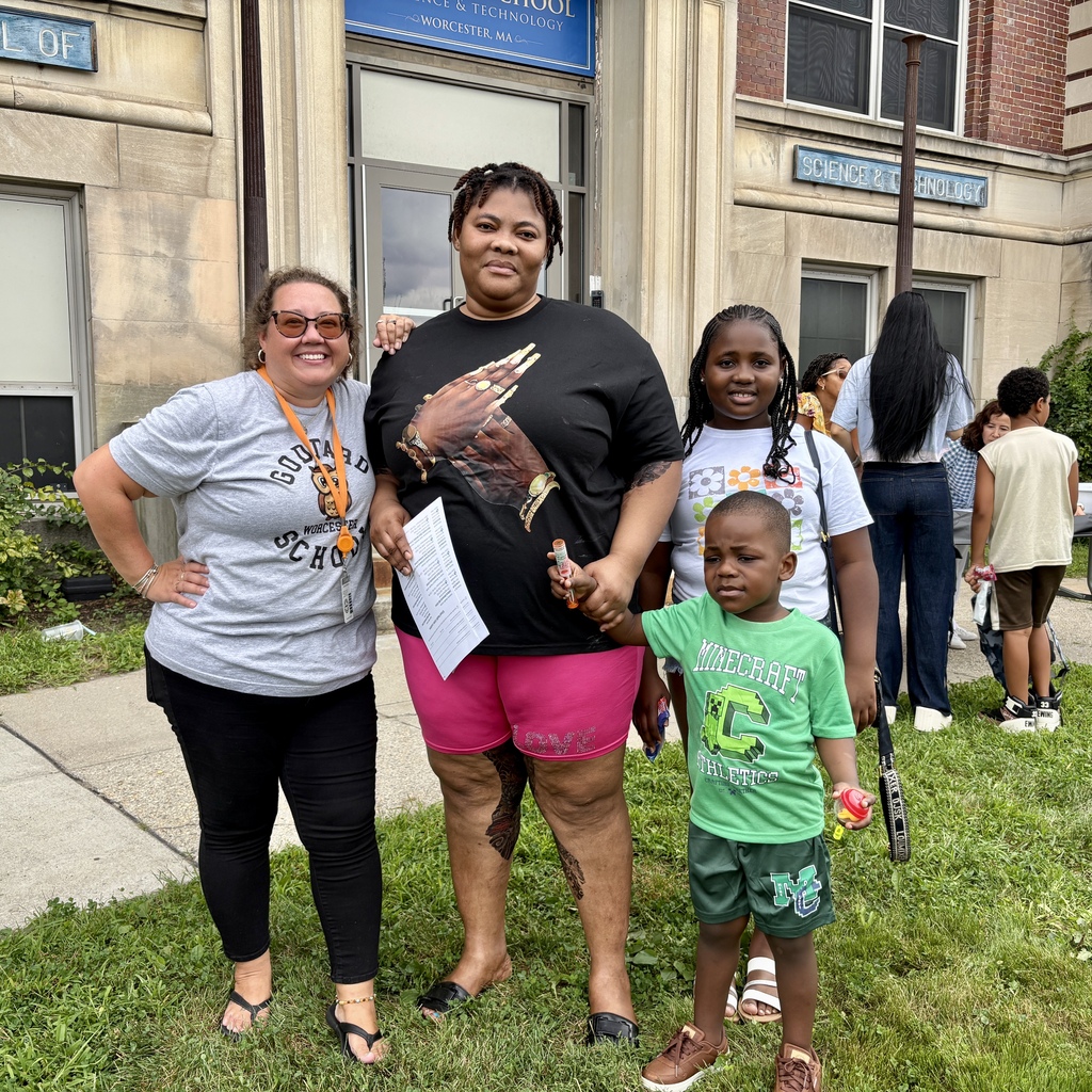 A group of people, including children and adults, stand outside a building with signs reading "SCHOOL OF SCIENCE & TECHNOLOGY WORCESTER, MA".