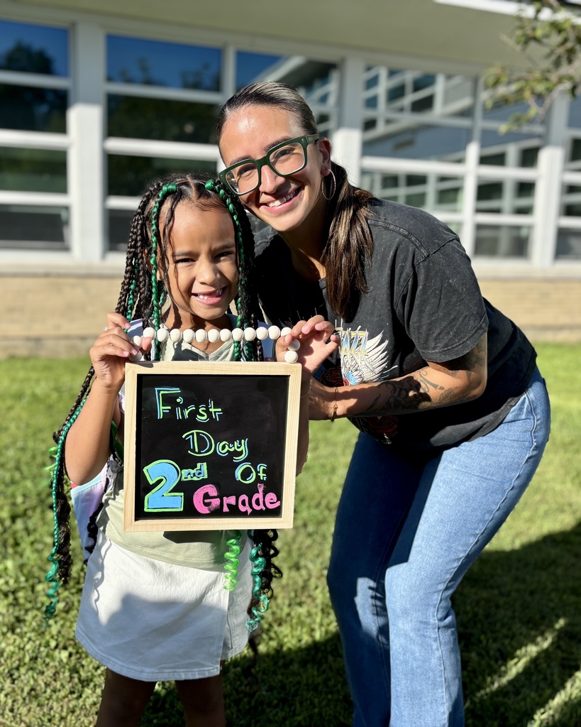 A student and her mother hold a sign that says "First Day of 2nd Grade."