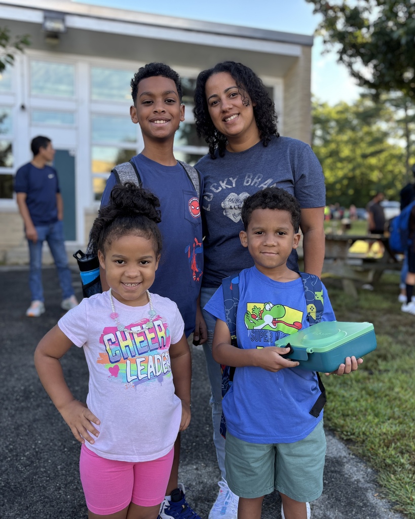 Three young students stand alongside their mother on the first day of school.