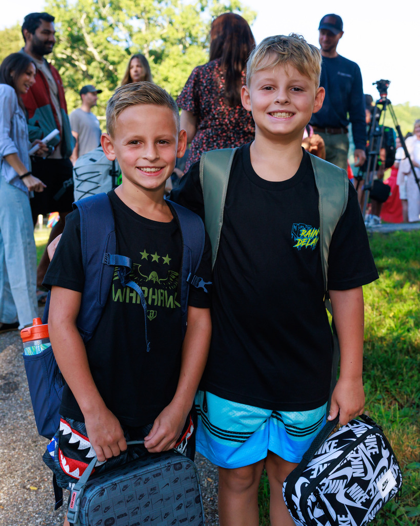 Two brothers stand side by side on the first day of elementary school.