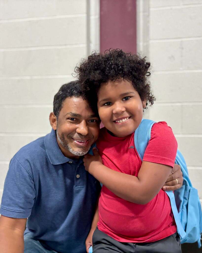 A student and his father stand together on the first day of Pre-K and Kindergarten.