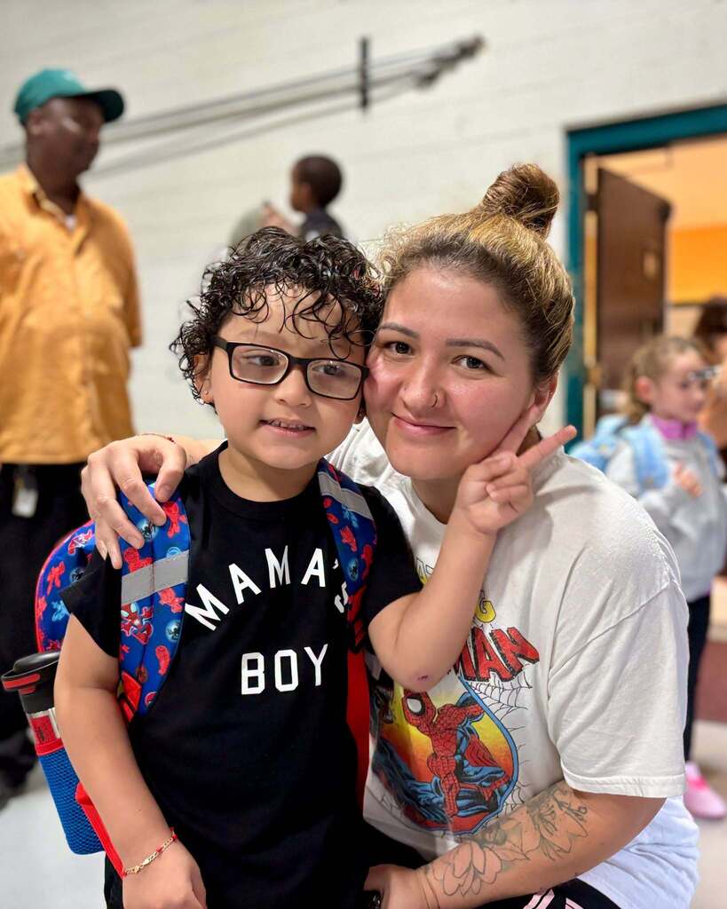 A student and his mother stand together on the first day of Pre-K and Kindergarten.