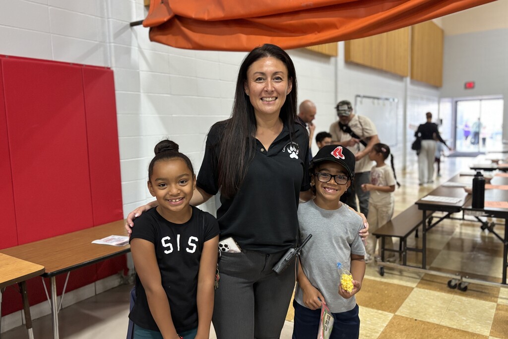 A smiling woman with long dark hair poses indoors with two young children, a girl and a boy.
