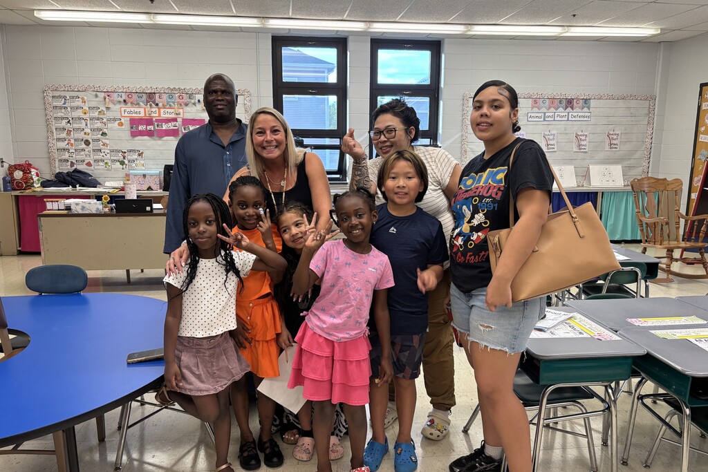A group of adults and children pose for a photo together inside a brightly lit classroom.