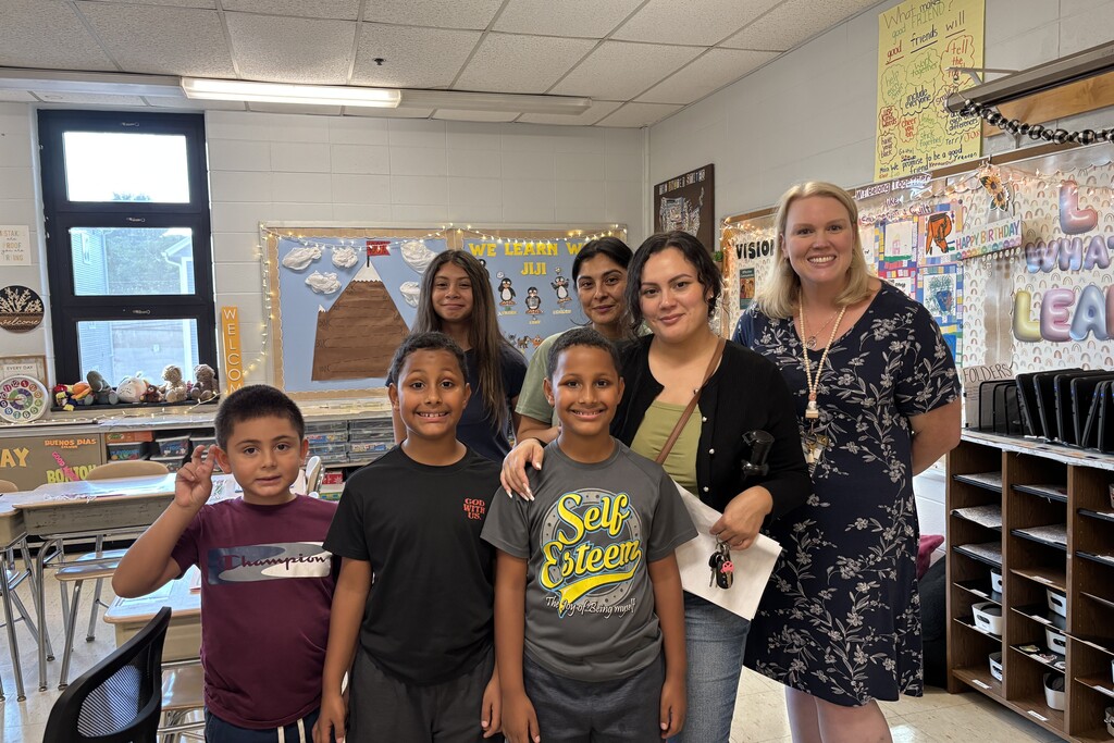A group of children and adults pose for a photo inside a brightly lit classroom.