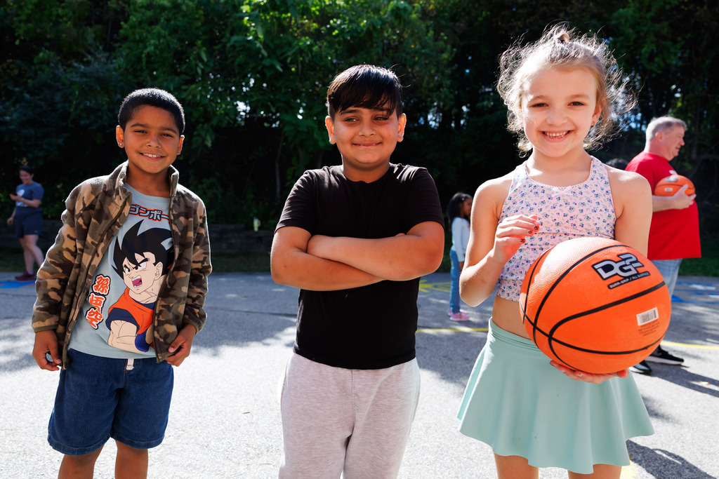 Three students stand side-by-side and smile, one of them is holding a basketball.