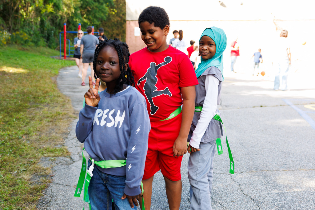 Three students pause from flag football to smile for a photo.