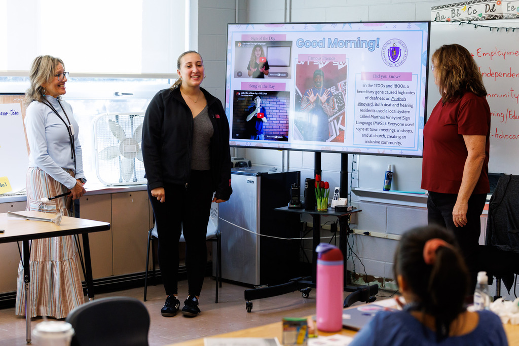 Three adults stand in front of the class during a lesson.