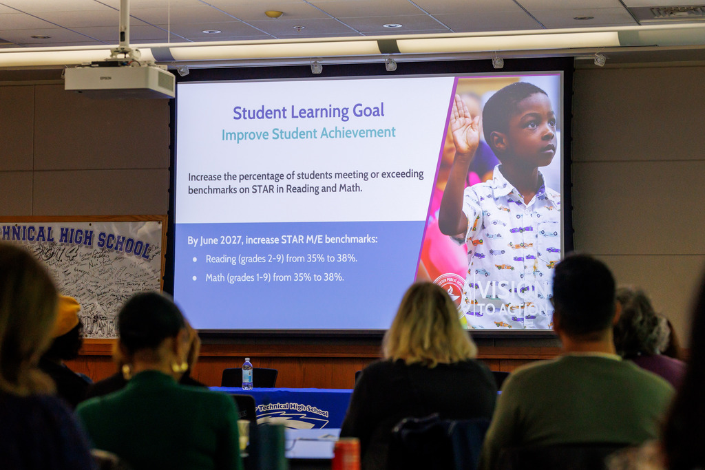 Spectators observe a presentation about student learning goals.