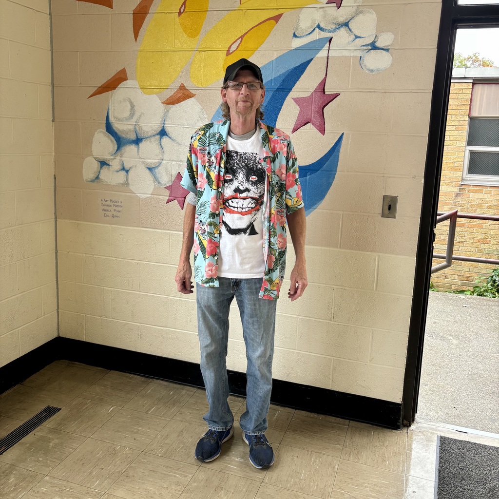 A man in a floral shirt and graphic t-shirt stands before a painted mural.