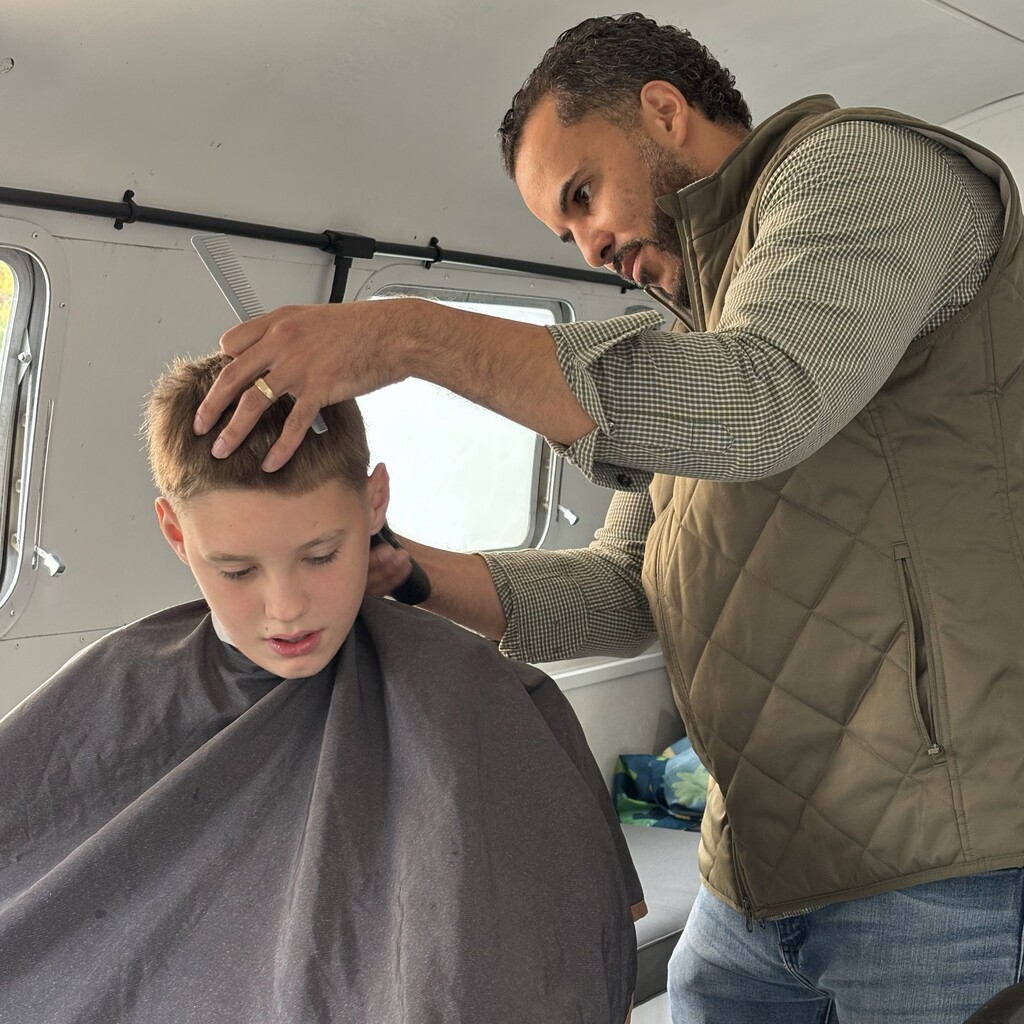 A man carefully cuts a young person's hair using a comb and clippers indoors.