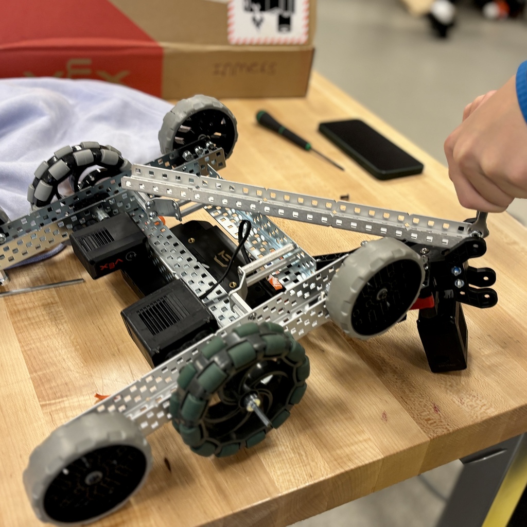 A student uses a tool to assemble a metal robotics kit on a wooden workshop table.