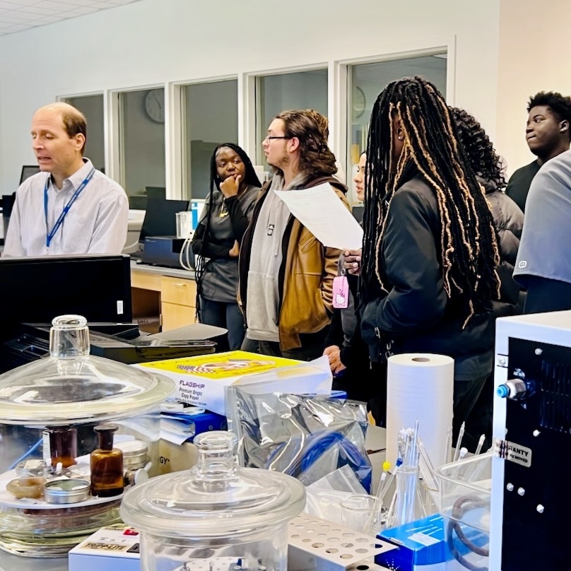 A group of diverse students and an instructor gather in a bright, modern laboratory setting.