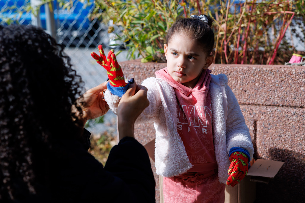 An adult helps a young student put on their gardening gloves.